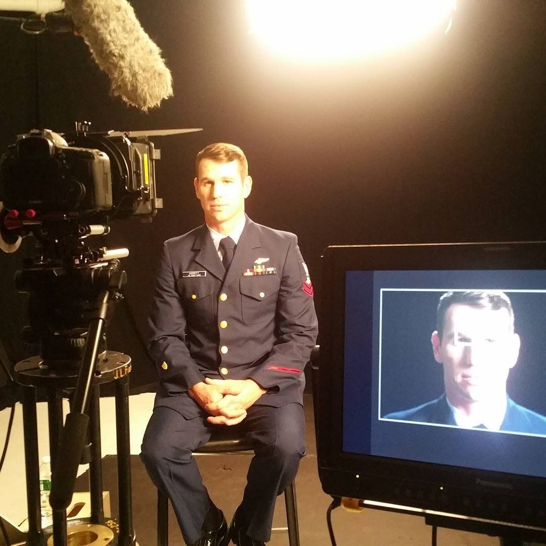 Man in uniform sitting for an interview, in front of a camera, with his image on a monitor.