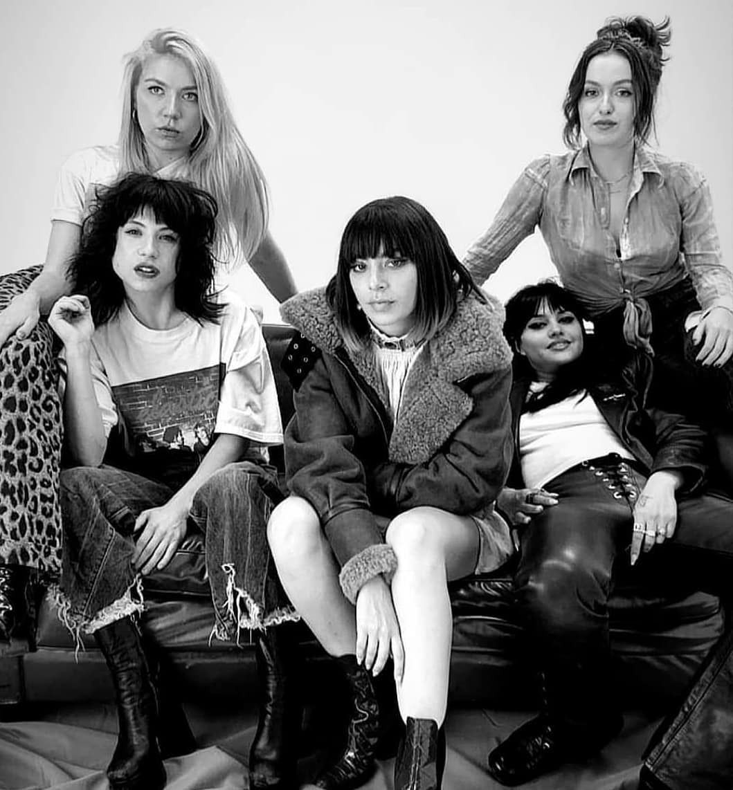 Group of five women seated on a dark sofa. Black and white photo; stylish and relaxed poses.