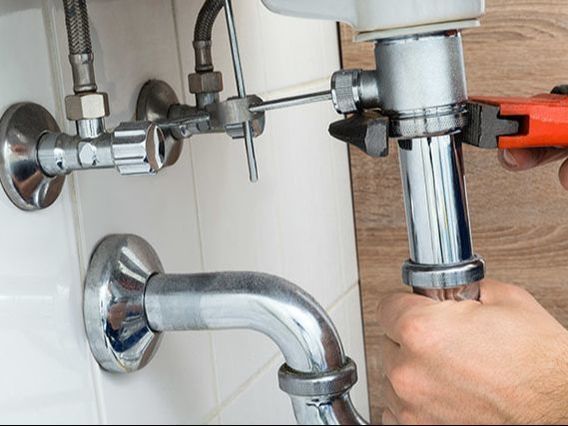 Plumber using a wrench to tighten a pipe under a sink.