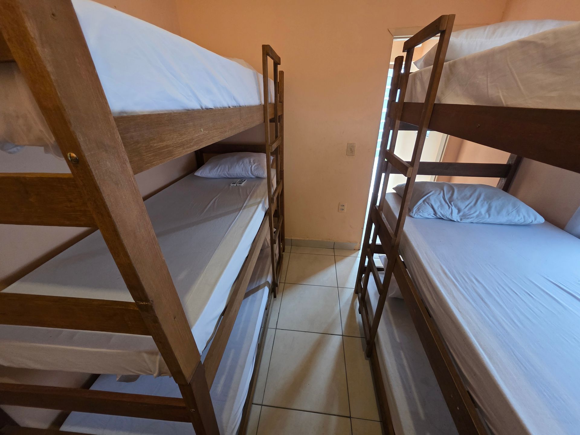 Duas camas de beliche de madeira em um quarto; camas vazias, paredes claras.