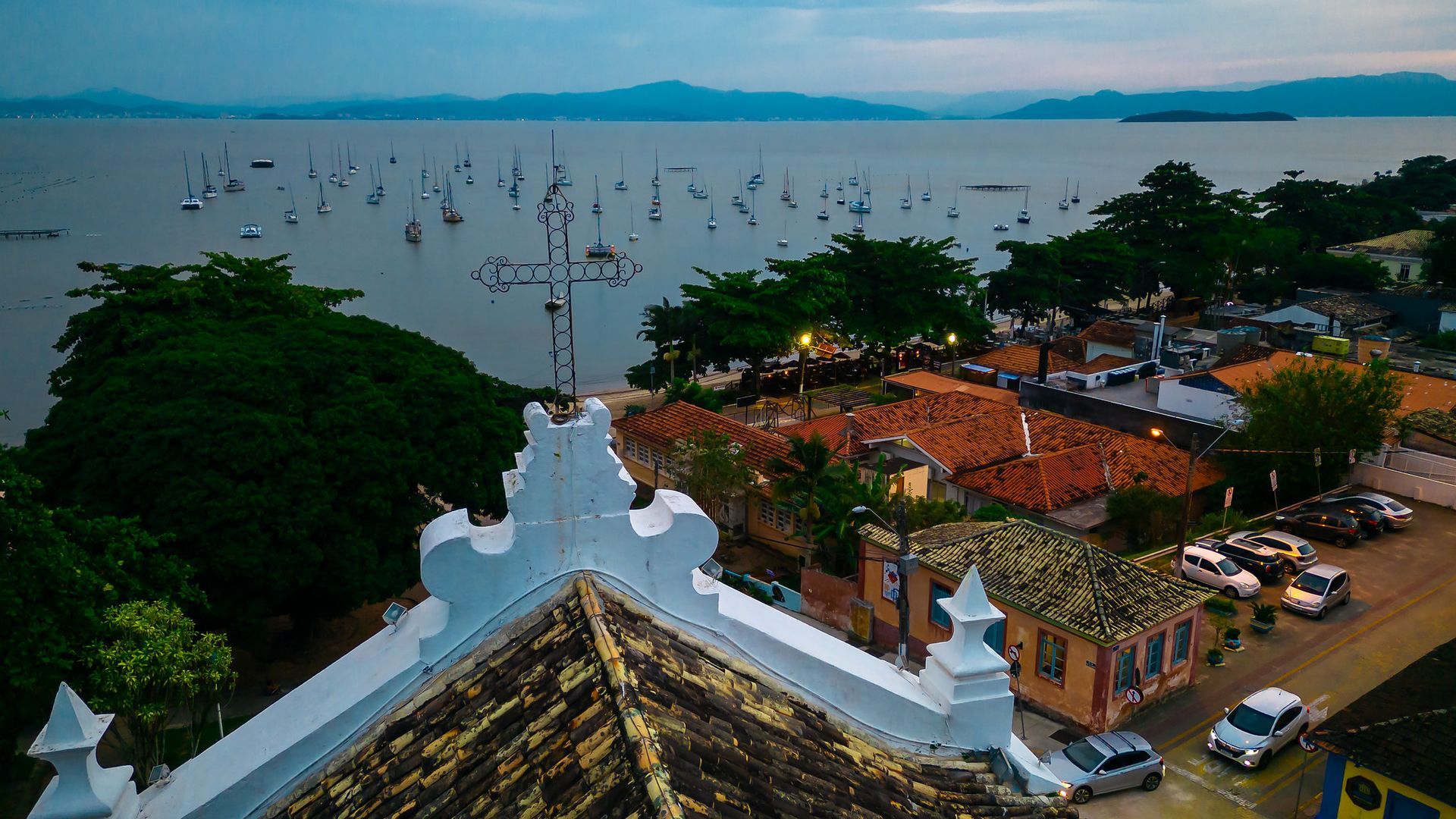 Vista de uma cidade costeira com barcos na água e montanhas ao longe.