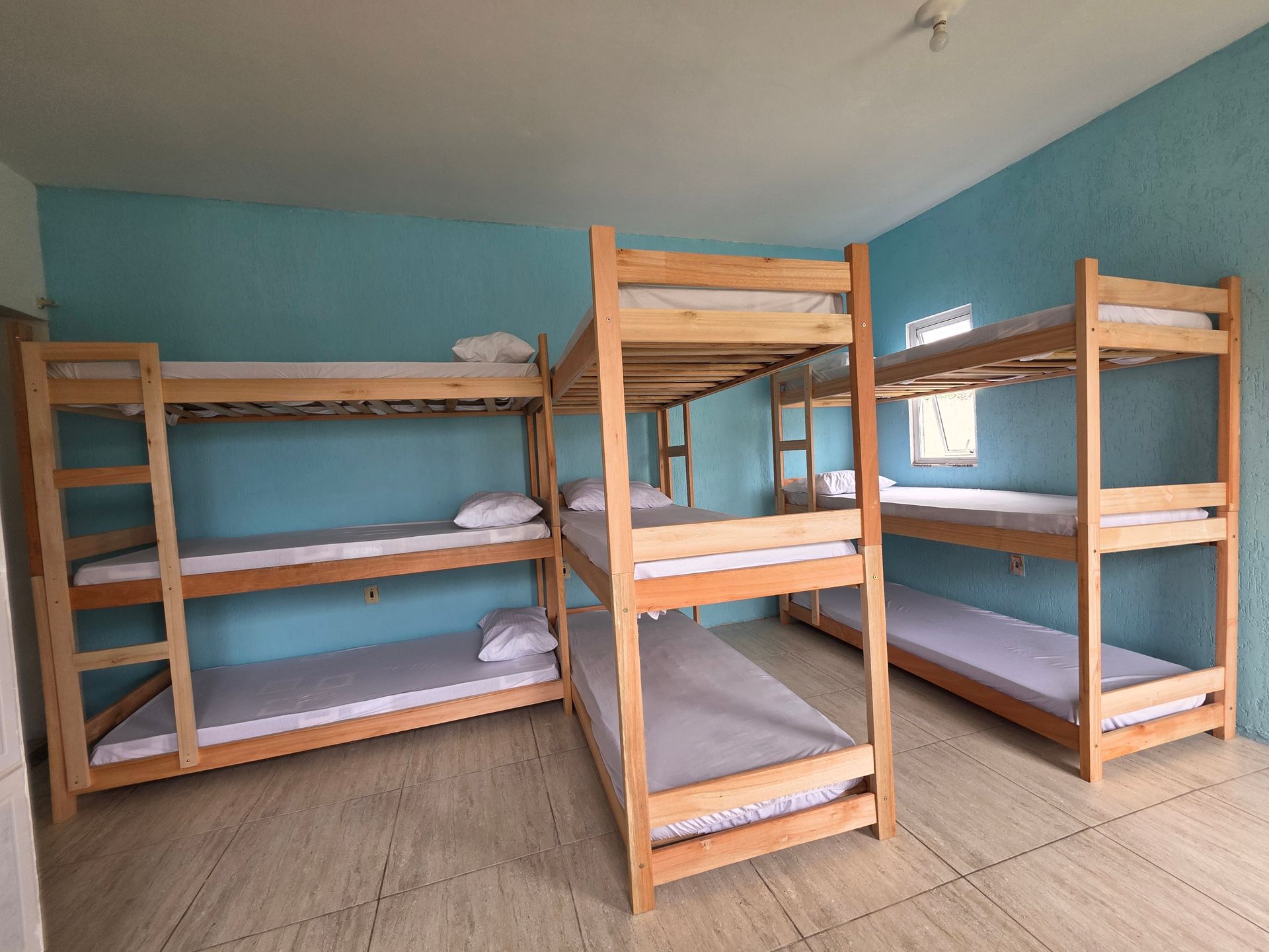 Quarto com vários beliches de madeira encostados em uma parede azul.