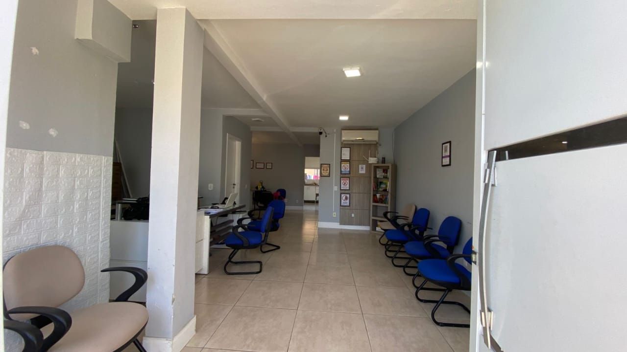 Interior de uma sala de espera com paredes cinzentas, cadeiras azuis e piso de azulejos brancos.