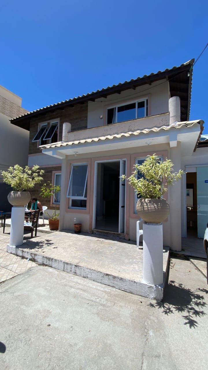 Casa bege de dois andares com porta da frente aberta, vasos de plantas e céu azul.