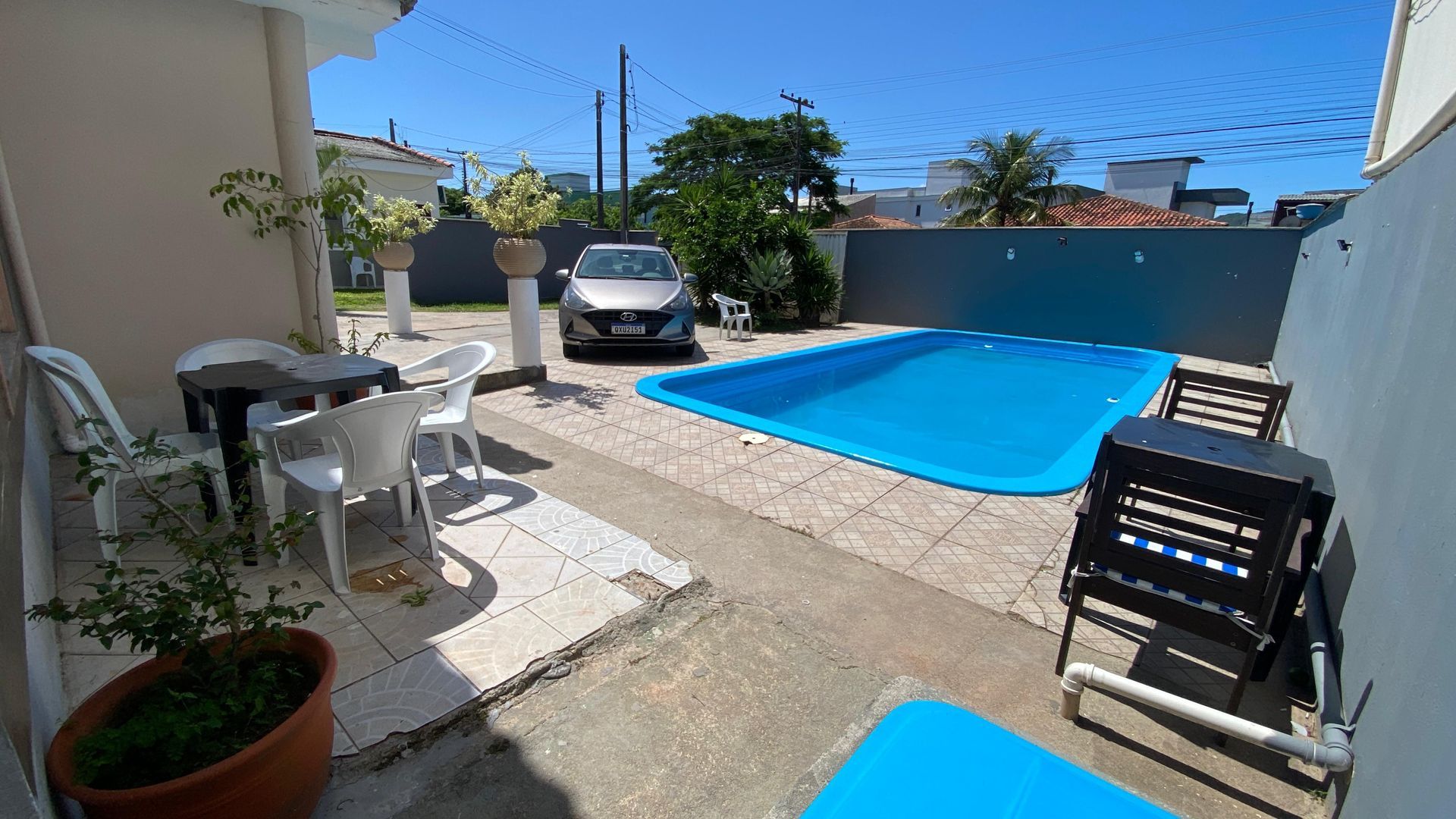 Quintal com piscina azul, móveis de jardim, um carro e céu limpo.