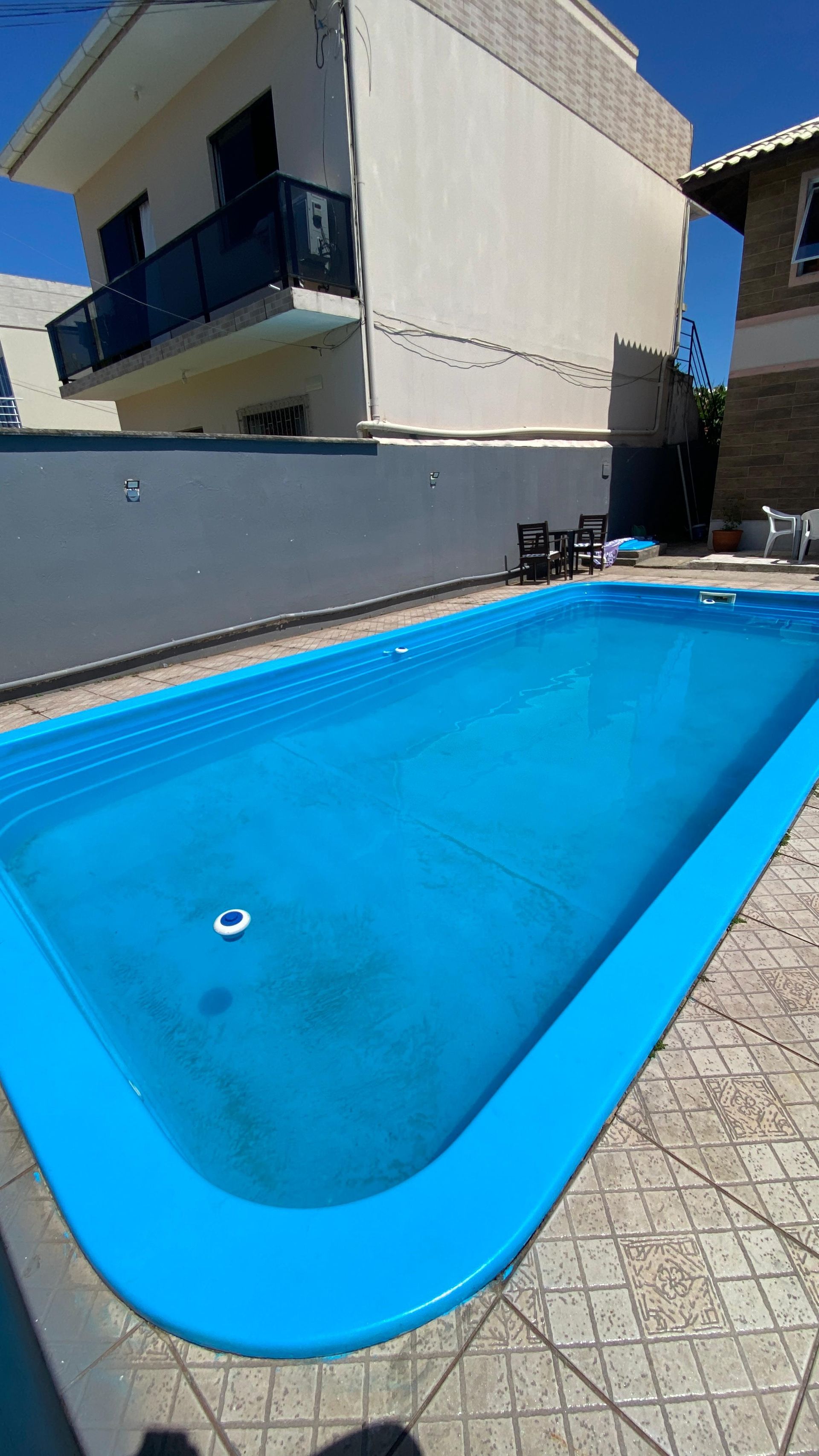 Piscina azul em frente a um prédio de vários andares sob um céu claro.