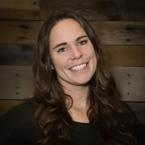 A woman with long hair is smiling in front of a wooden wall.