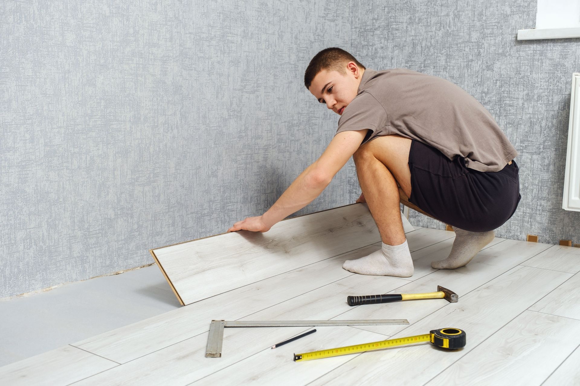 Young man installing laminate flooring in a room, placing a floorboard with measuring and cutting to
