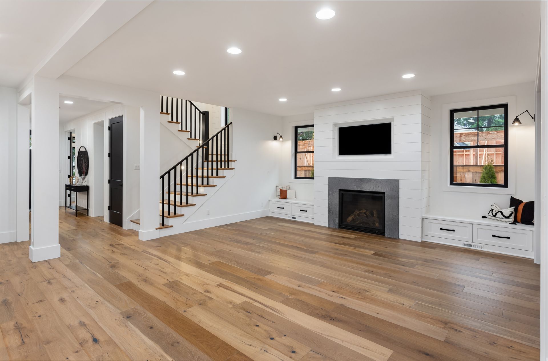 Bright empty living room with hardwood floors, white walls, staircase, fireplace, and recessed lighting