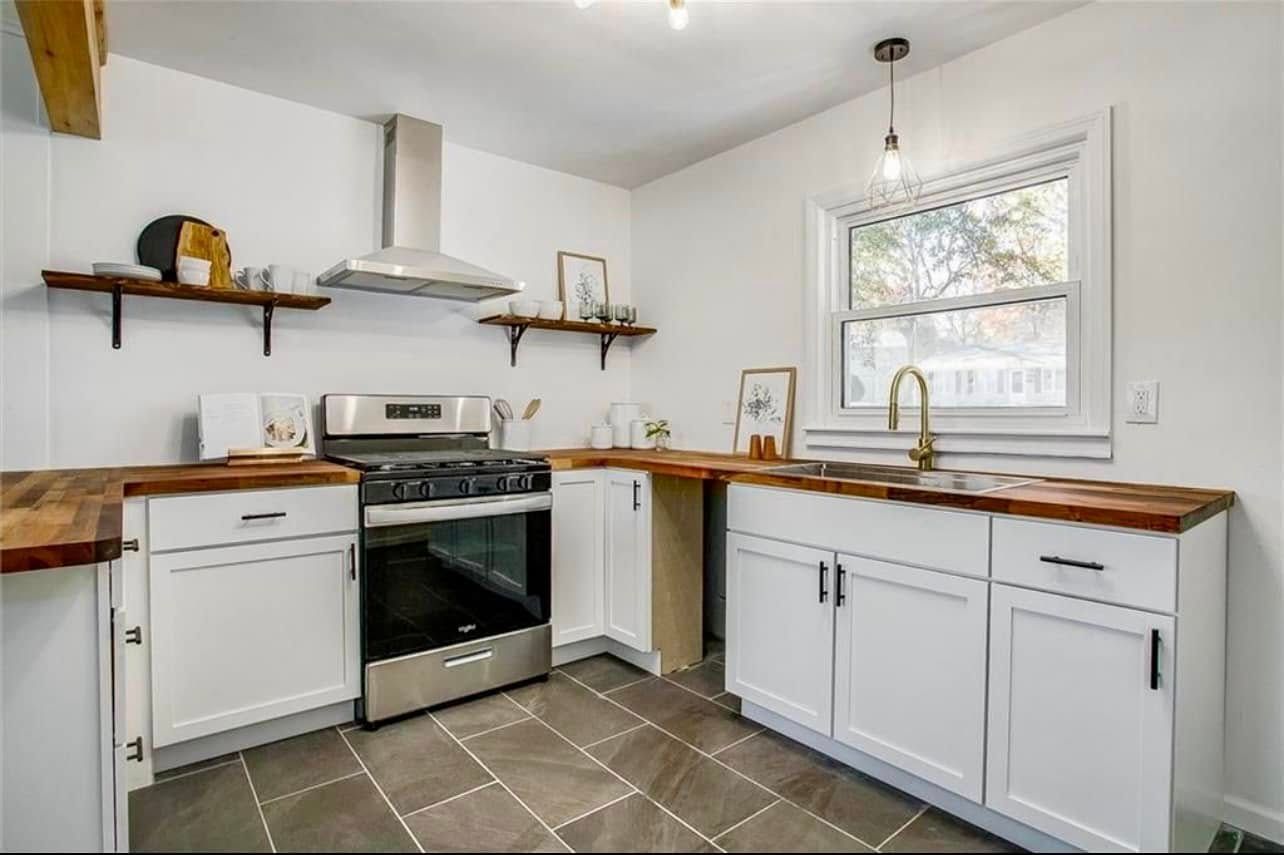 White kitchen with wooden countertops, stainless steel appliances, open shelving, and a window.