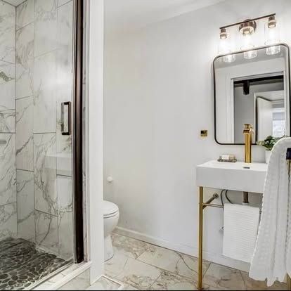 Modern bathroom with marble shower, white walls, floating sink, and gold accents.