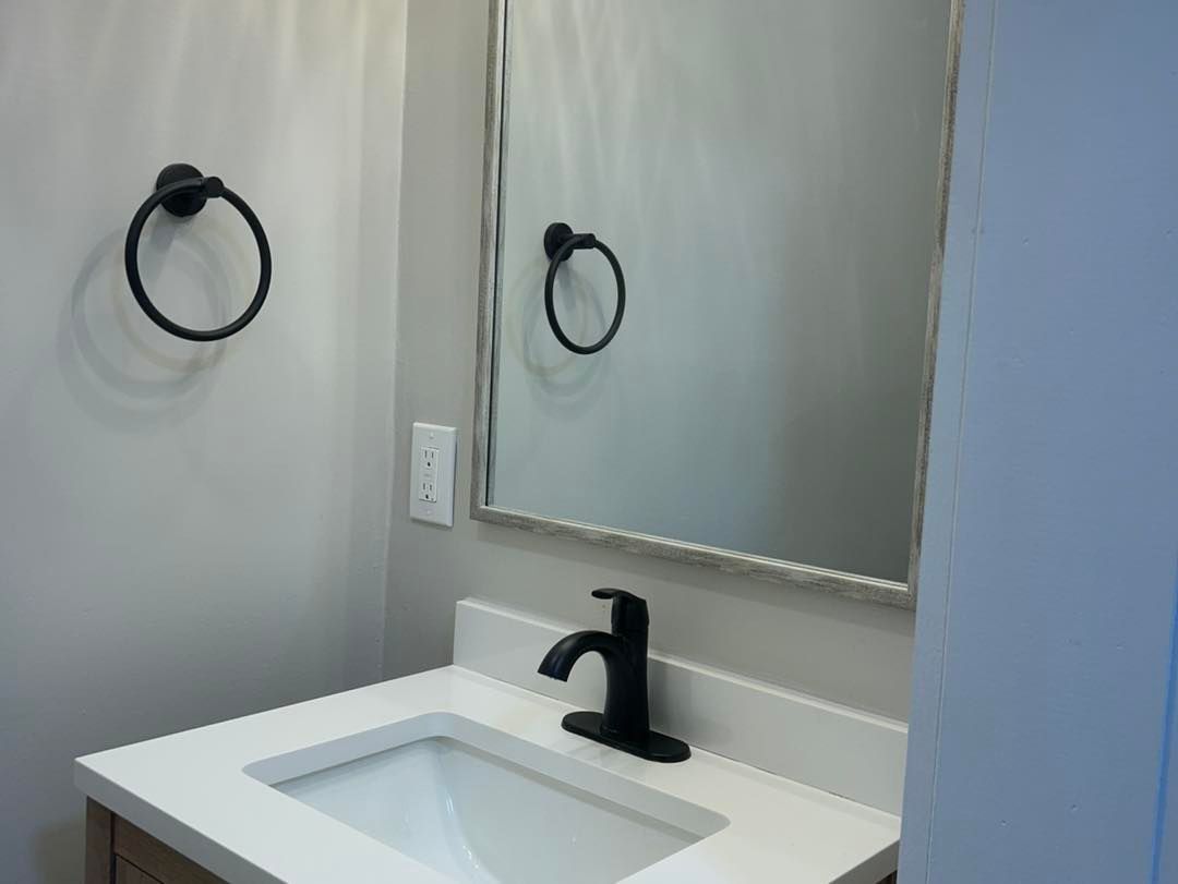 A bathroom with a sink , mirror and towel rings