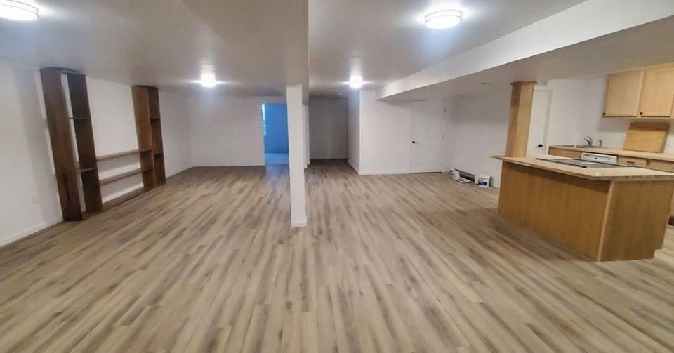 A large room with a wooden floor and a kitchen in the background.