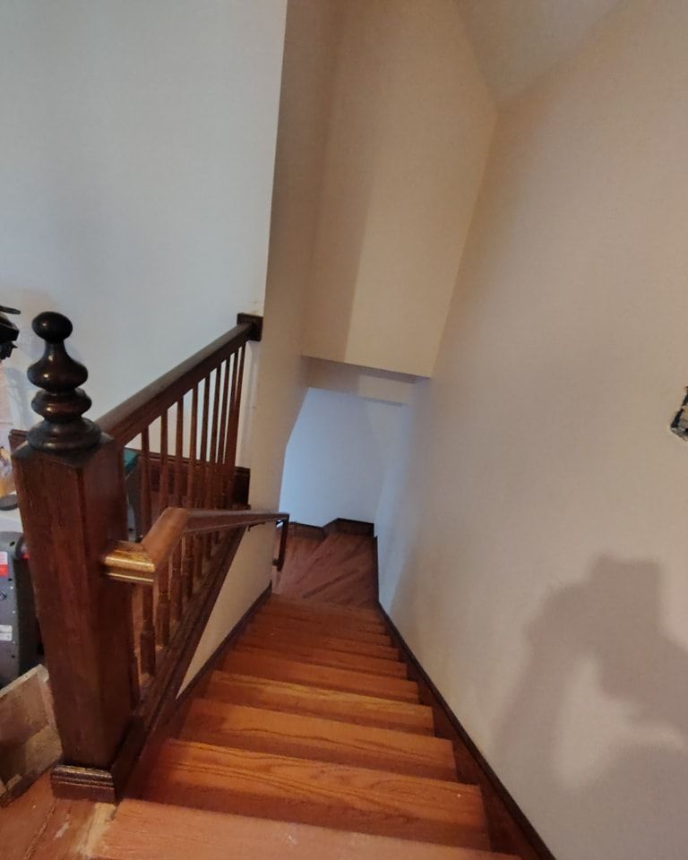 A wooden staircase with a wooden railing and a white wall.