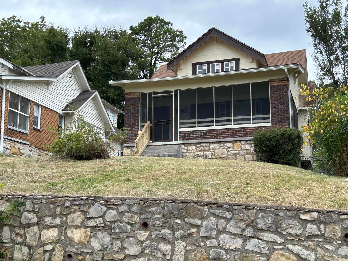 A house with a screened in porch is sitting on top of a hill next to a stone wall.