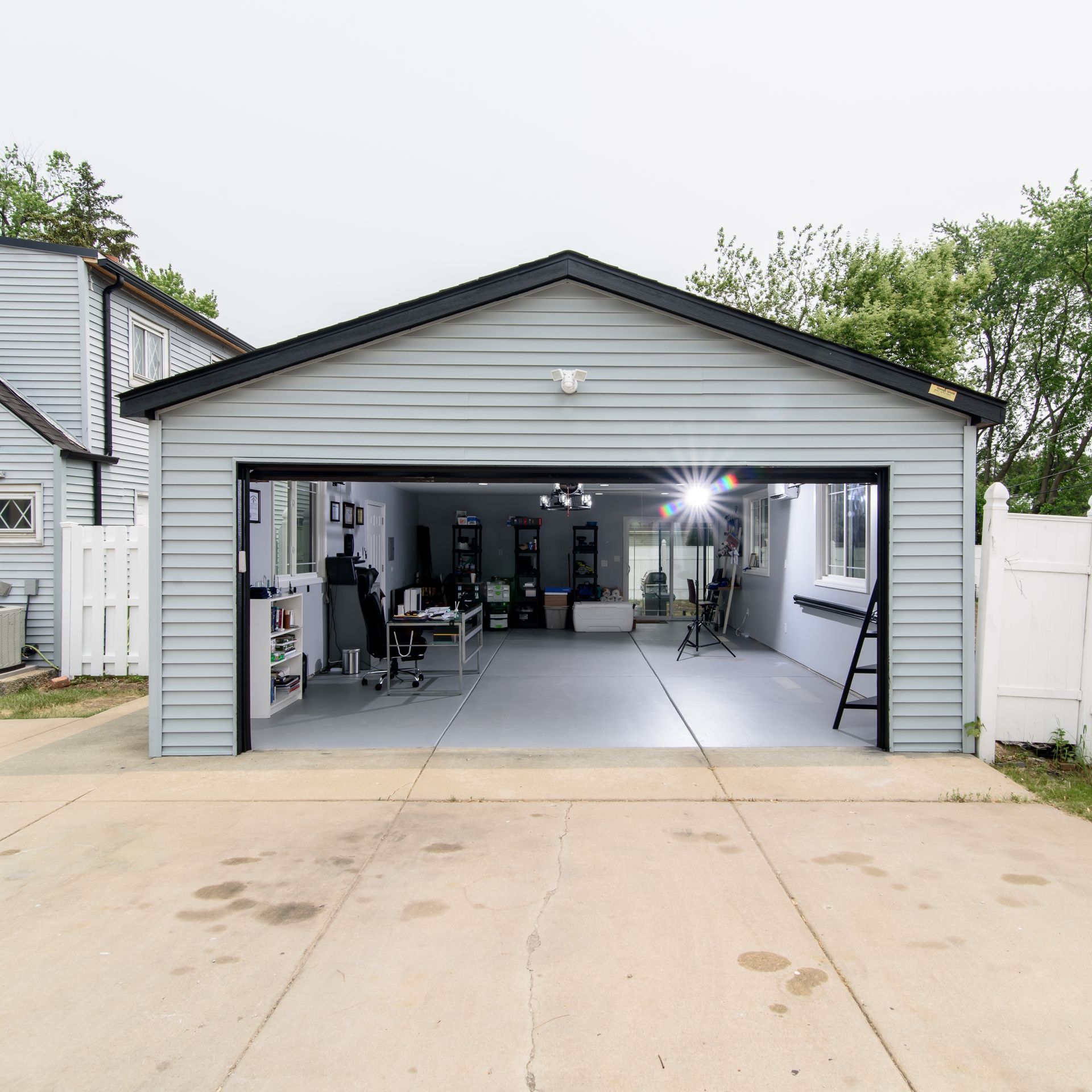 Garage with open door, converted into a studio. Grey siding, concrete driveway, and interior with equipment.
