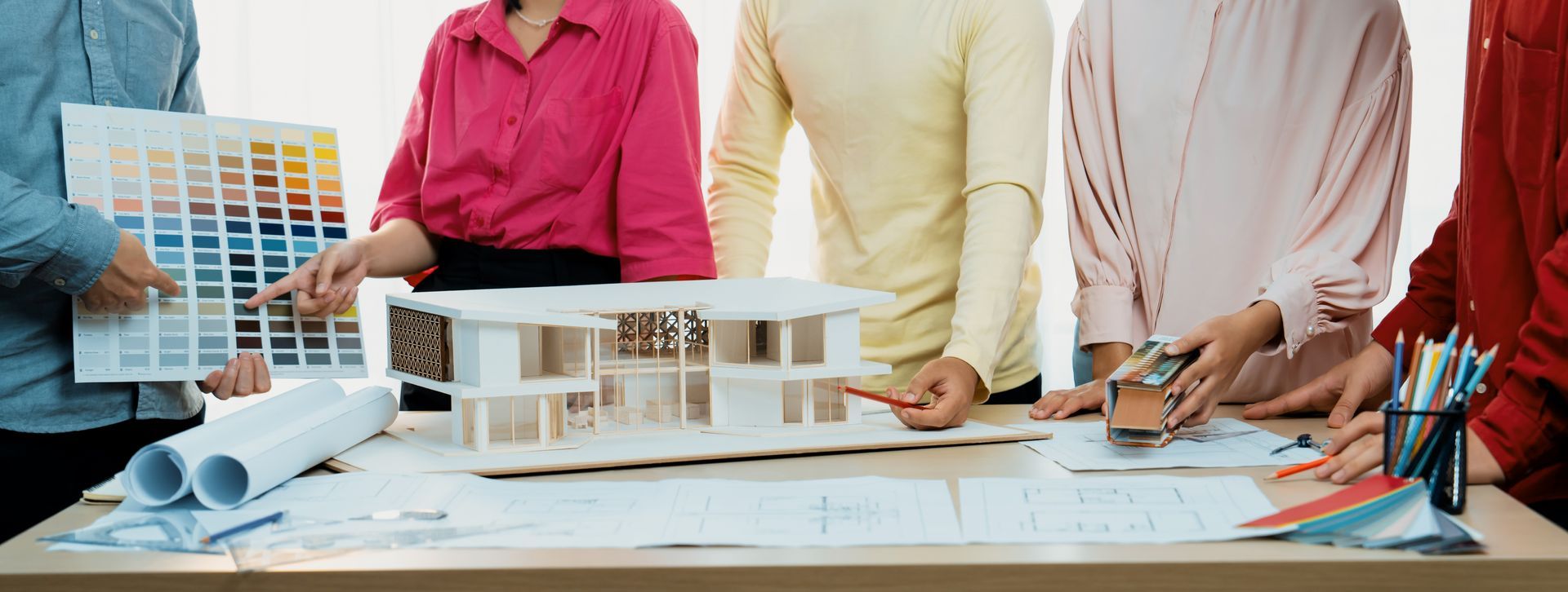 Team of architects reviewing house model, color swatches, and blueprints at a table.