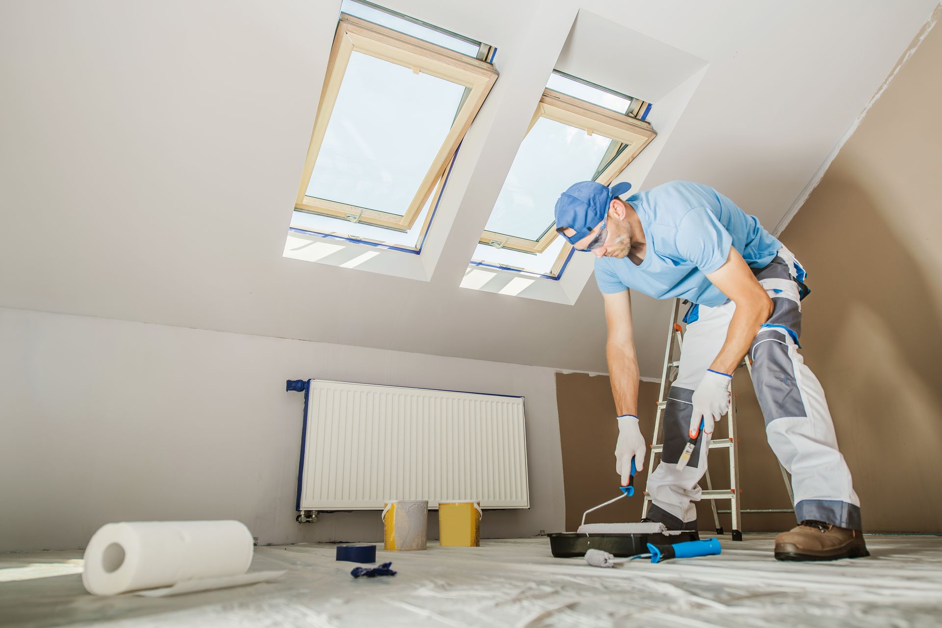 A man is painting the floor of a room with a roller.
