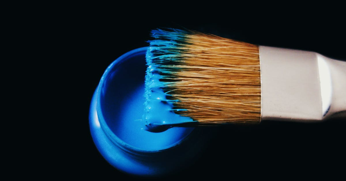 A paintbrush with blue paint dripping into a paint can