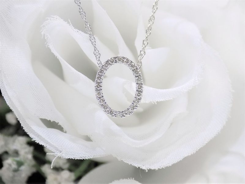 Silver necklace with diamond oval pendant on a white rose.