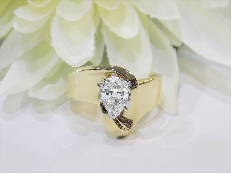 Gold ring with pear-shaped diamond on white surface