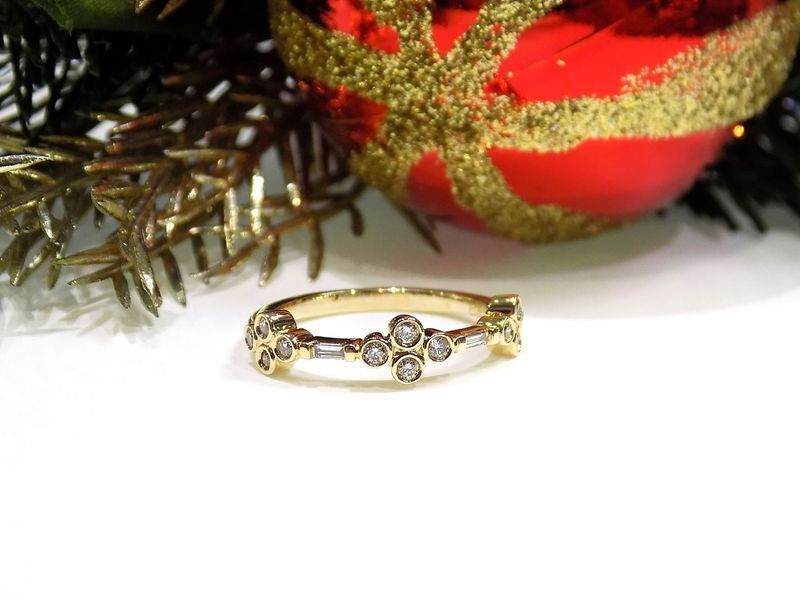 Gold ring with diamonds in front of a red and gold ornament and Christmas branches