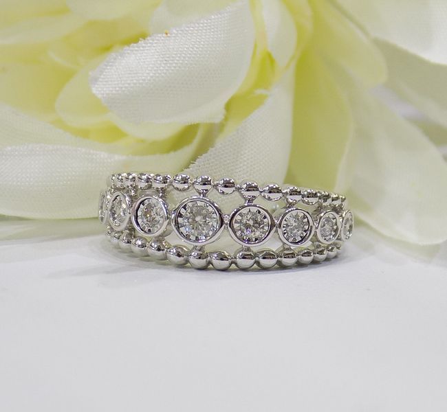 Diamond ring with a beaded design, resting on a white surface