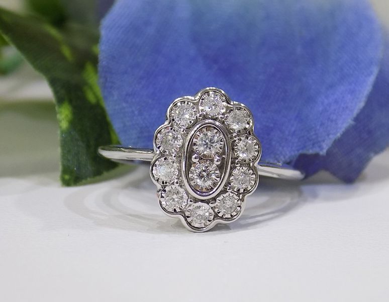 Diamond ring with an oval cluster of small diamonds, set against a blue flower.