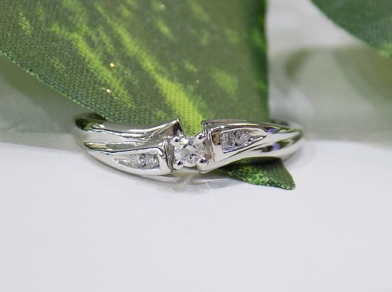 Diamond ring on a white surface, framed by green leaves.