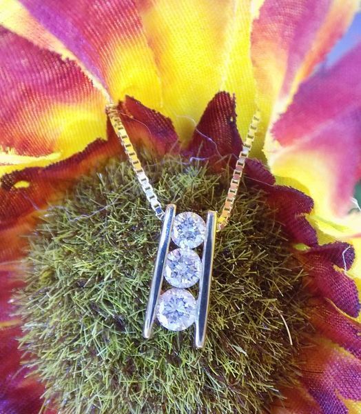 Diamond pendant necklace with three stones set against a colorful flower background