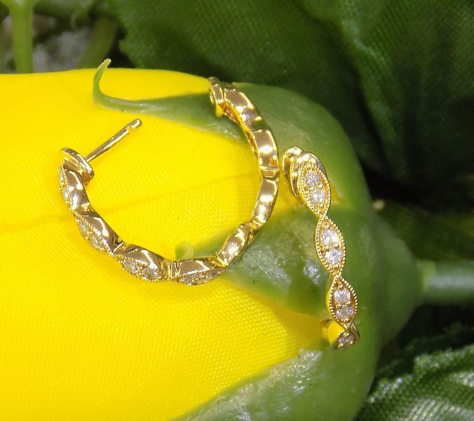 Gold hoop earrings with small diamonds on a yellow and green surface