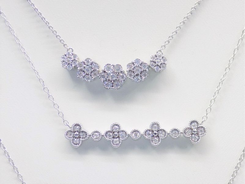 Two silver necklaces with diamond clusters and clover designs
