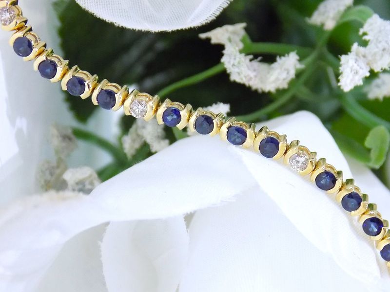 Gold bracelet with blue and white gemstones on white floral background