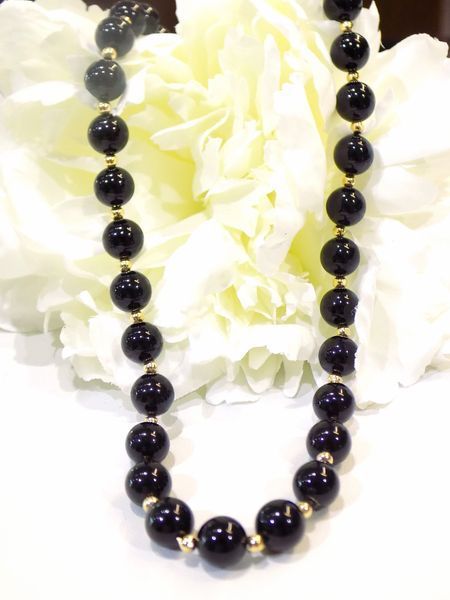 Black beaded necklace with gold spacers in front of a white floral arrangement