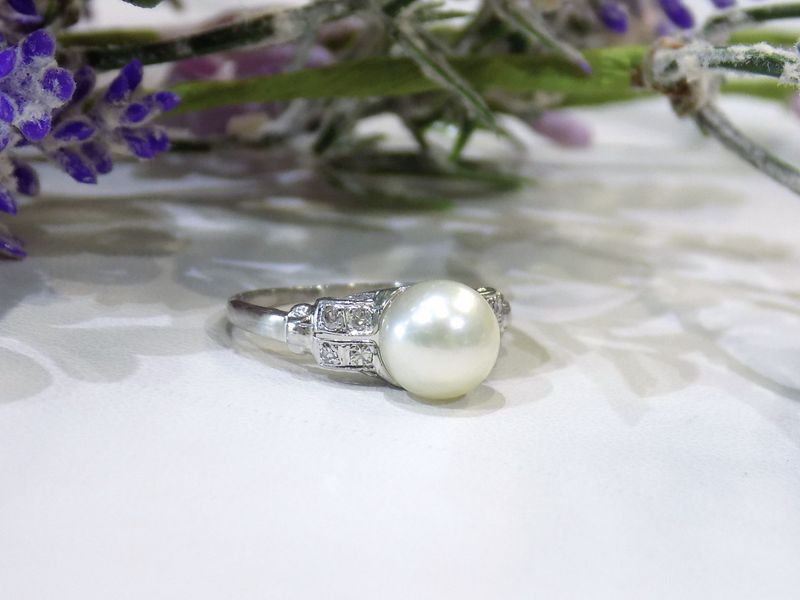 Pearl ring with small diamonds set on a white surface with lavender flowers