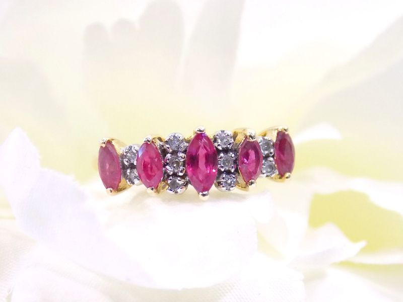 Gold ring with oval red stones and diamond accents on a white floral background