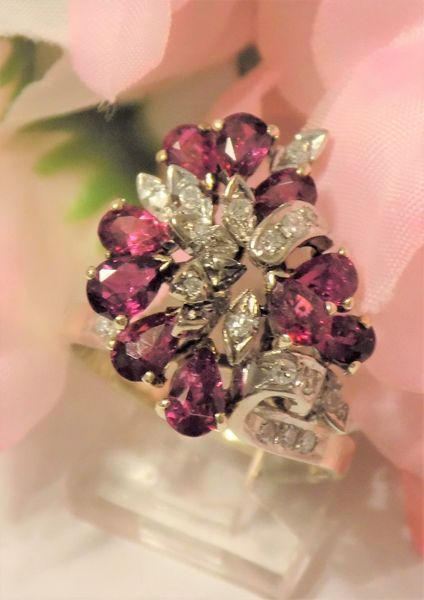 Gold ring with cluster of red oval stones and diamonds against pink flowers.