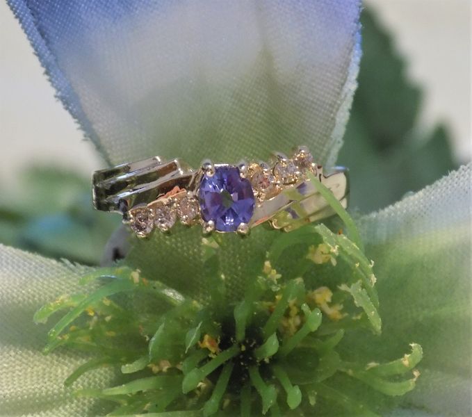 Ring with a purple oval stone and small surrounding white stones, set on a green flower.