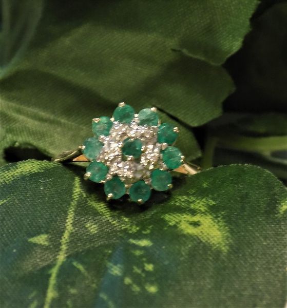 Emerald and diamond cluster ring on a dark green leaf