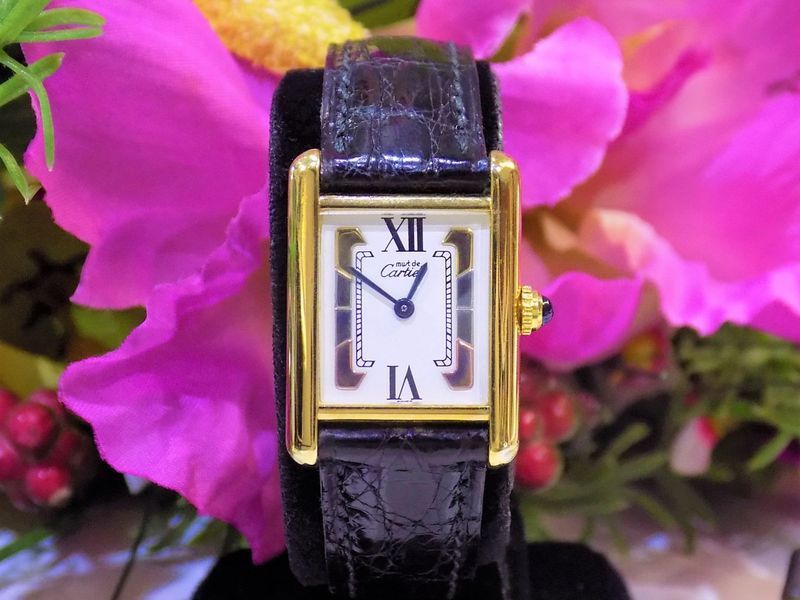 Gold cartier tank watch with a black strap on a display stand