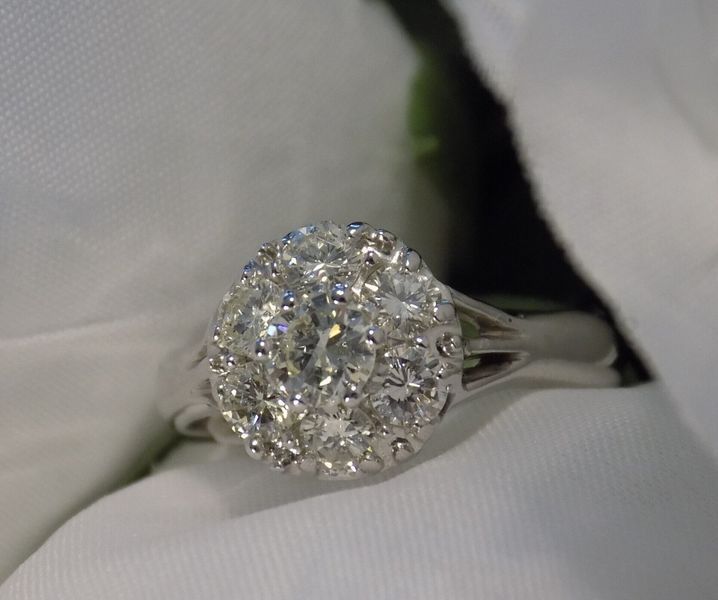 Diamond cluster engagement ring on white fabric.