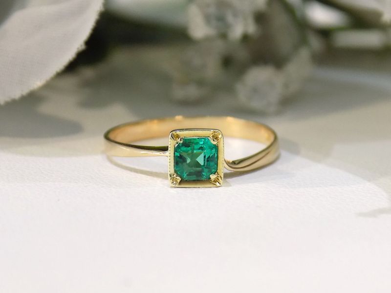 Gold ring with square-cut emerald gemstone on a white surface