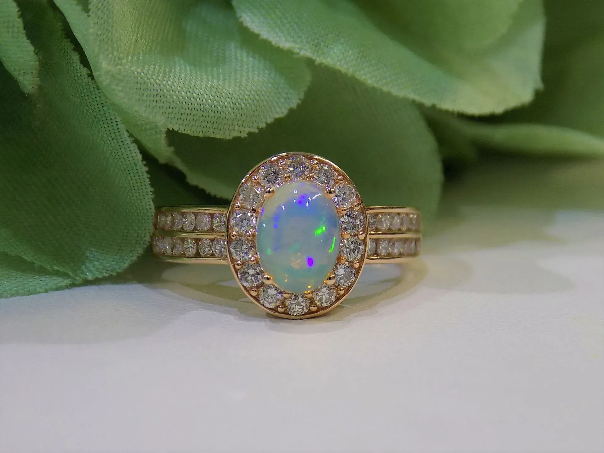 Oval opal ring with a diamond halo and band on a white surface