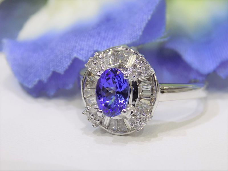 Oval tanzanite ring with a halo of diamond baguettes, set against blue petals