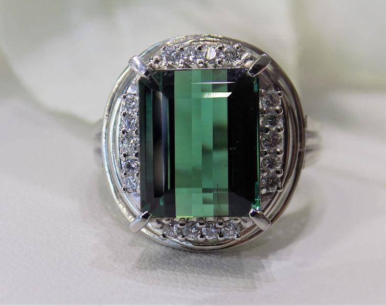 Green emerald-cut gemstone ring with surrounding small diamonds in a silver setting.