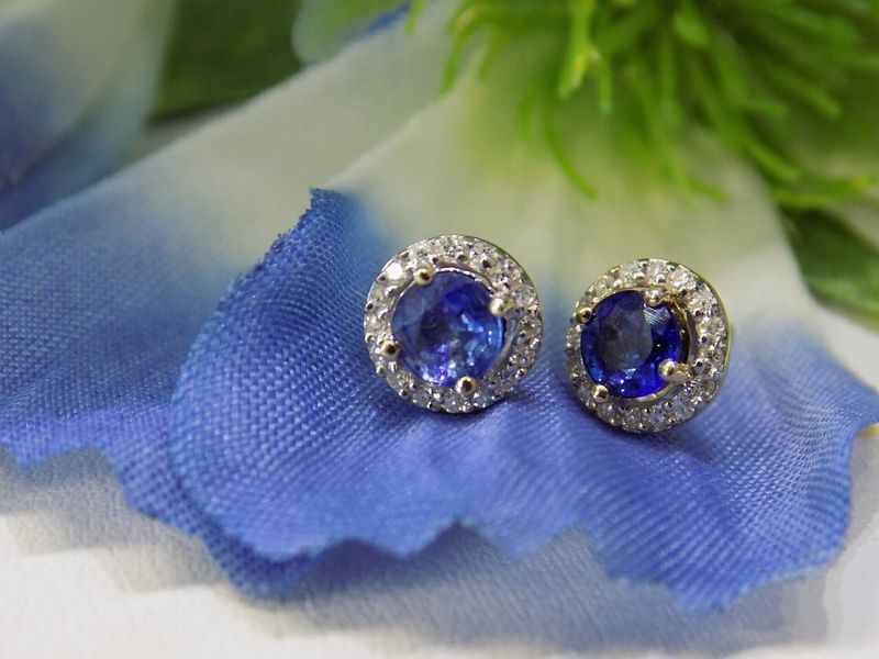 Blue sapphire and diamond halo stud earrings on a blue cloth