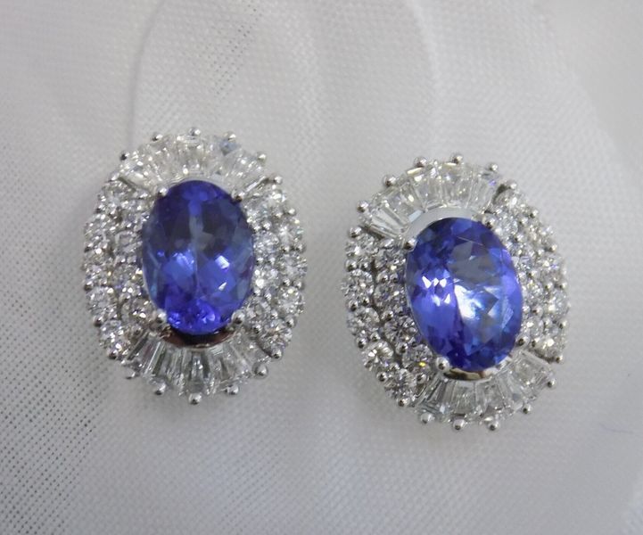 Pair of oval blue gemstone stud earrings with diamond halo on white fabric