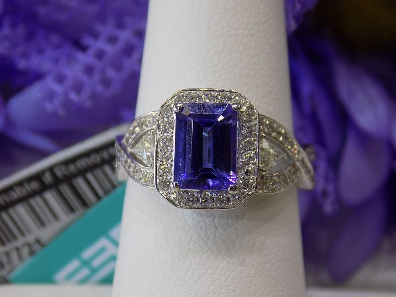 Emerald-cut purple gemstone ring with a diamond halo on a white ring stand