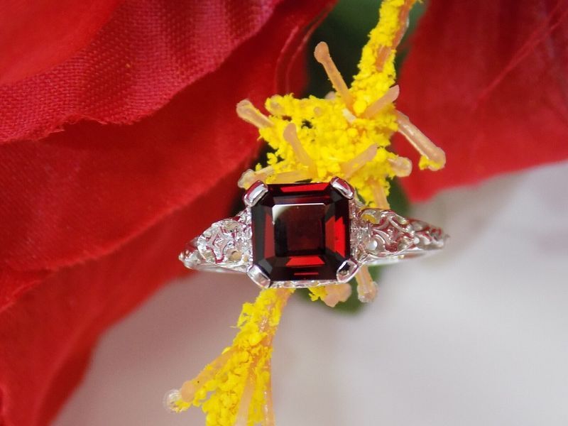 Silver ring with a square, red gemstone set on a yellow flower against a red petal