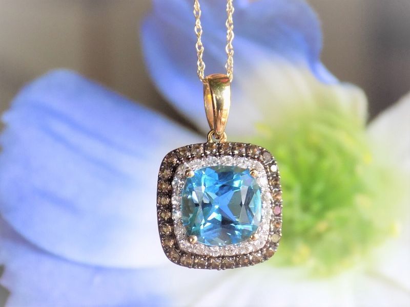 Gold pendant with blue gemstone, surrounded by brown and white gems, on a gold chain